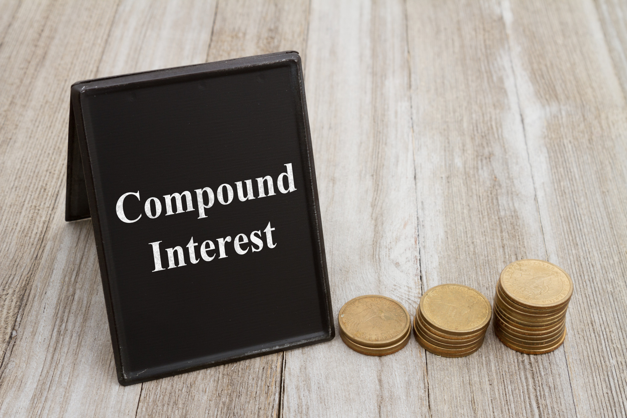 Understanding compound interest, Retro freestanding chalkboard  with gold coins on weathered wood with text Compound Interest